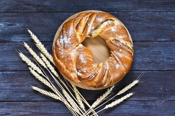 Round cinnamon bread on a wooden board, on a wooden background with ears of wheat. Still life, rustic style. Top view with copy space