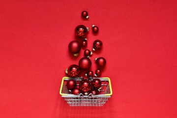 Shopping basket with red Christmas balls on red background with copy space. Banner. Christmas sale, discounts, holiday shopping and buying gifts. New Year concept. Flat lay composition