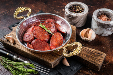 Turkish fried sausage sucuk in a pan. Dark background. Top view