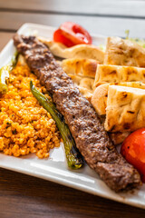 Turkish Adana kebab on a plate with marinated peppers,  bread and rice pilaf. Top view