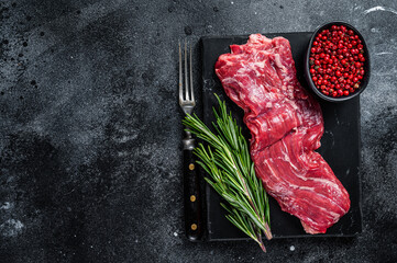 Raw machete skirt beef meat steak on marble board. Black background. Top view. Copy space