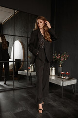 Graceful adult woman with stylish waved hairstyle wearing trendy black suit poses in the luxurious interior