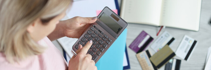 Woman sitting on floor near scattered bank cards and counting on calculator