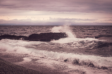 sea waves with splashes and foam wash over the rocky stones