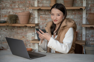 Portrait of pretty young Chinese Asian businesswoman wearing classic clothes in cafe restaurant office uses her mobile phone and laptop. Freelance worker using internet in coffee shop to make the job.