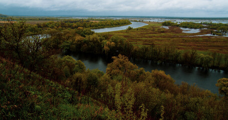 Beautiful summer landscape on a cloudy day. View from the hill to the winding river in rainy weather. View from  height of the meadow flooded after the flood in spring. Nature and landscape in Europe