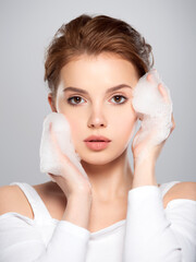 Beautiful face of young caucasian woman with perfect healthy skin, isolated.   Pretty white model caring of face.  Skin care concept. Girl moistens her face.  Woman with soap foam street.