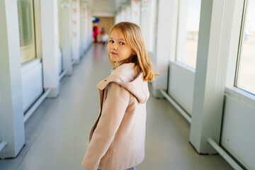 a little girl in a coat walks and look back down the corridor to board a plane. 