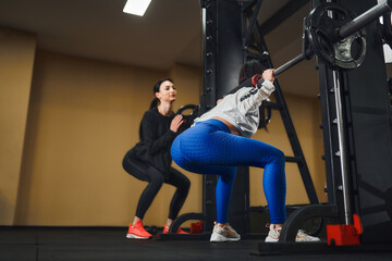 Fototapeta na wymiar Young caucasian woman working out legs with barbell In gym with instructor. Personal female trainer