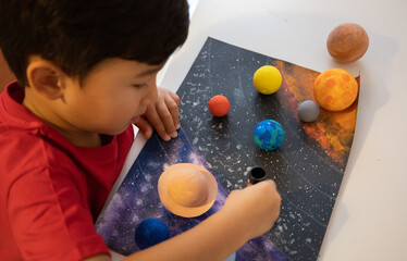 Preschooler glue a 3D planets on list of paper. Homeschool education. Handmade solar system. Studying Astronomy objects.