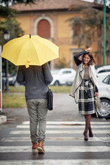 Some handsome and elegant young woman and man pass each other at a pedestrian crossing on a rainy day. Walk, rain, city
