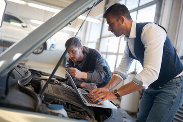 Naklejka na ściany i meble Men mechanics check the diagnostics on laptop at car