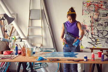 A young female artist is pouring the paint over canvas in her studio. Art, painting, studio