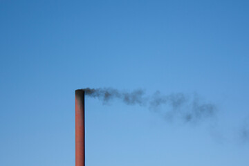 Release of harmful chemicals and substances into the atmosphere. Black smoke from the chimney is red against a clear, blue sky. Environmental pollution.
