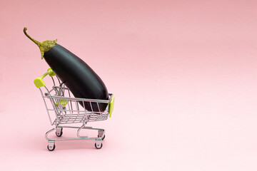 Shopping cart with eggplant on a pink background. Grocery and grocery store concept.