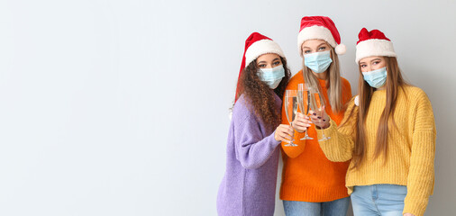 Beautiful young women in Santa hats, with medical masks and glasses of champagne on light background with space for text