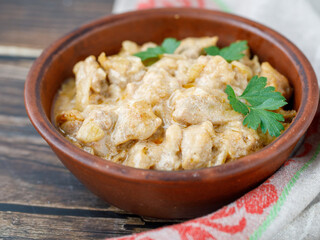 chicken fillet stewed in sour cream sauce with onion and garlic on ceramic plate with parsley leaf on wooden background, side view