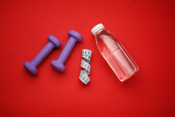 Dumbbells, bottle of water and measuring tape on red background
