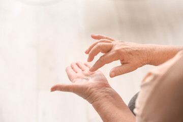 Elderly woman applying cosmetic cream onto her hands at home