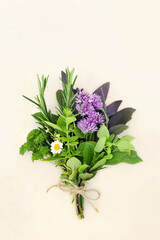 Fresh herb posy tied with string for drying and used in food seasoning and herbal medicine to treat various illnesses. On cream background, flat lay, top view.