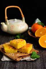 A picture of an orange cake with a teapot and pieces of orange on a dark background