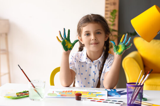 Cute little girl with hands in paint at table