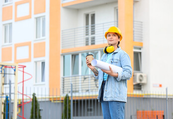 Female construction worker with house plan and cup of coffee outdoors