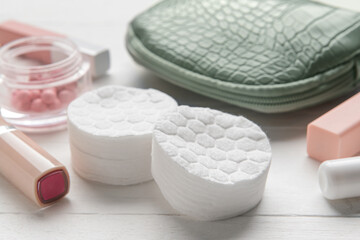 Stacks of soft cotton pads and cosmetics on white wooden table, closeup
