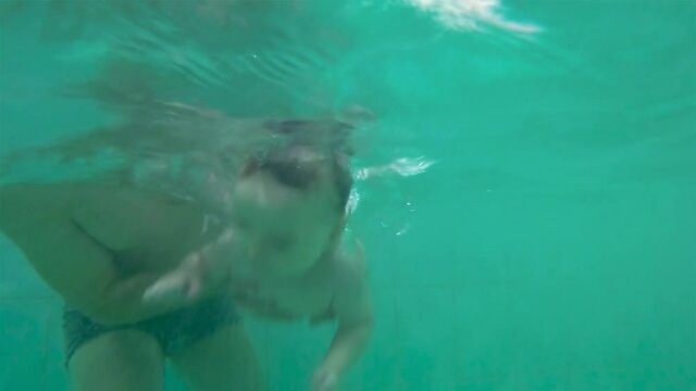 8-month Baby boy is diving with the support of his father in the swimming pool. Slow motion.