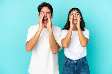 Young mixed race couple isolated on blue background shouting and announcing something