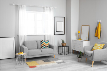 Fototapeta premium Interior of light living room with grey sofa, chest of drawers and blank frames