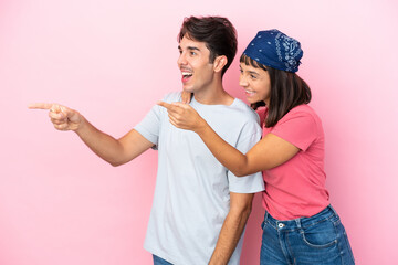 Young couple isolated on pink background presenting an idea while looking smiling towards