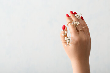 Female hand with stylish rings and gypsophila flowers on light background