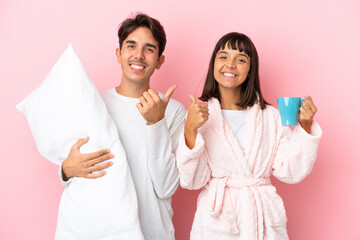 Young couple in pajamas isolated on pink background giving a thumbs up gesture with both hands and smiling