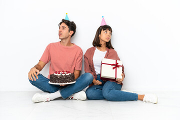Young mixed race couple celebrating a birthday sitting on the floor isolated on white background nervous and scared