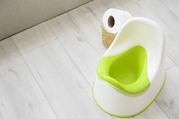 White potty and basket with toilet paper roll on grey wooden floor