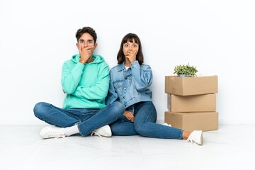 Young couple making a move while picking up a box full of things sitting on the floor isolated on white background covering mouth with hands for saying something inappropriate