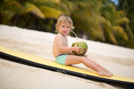 Happy funny little preschool kid boy drinking coconut juice on ocean beach.