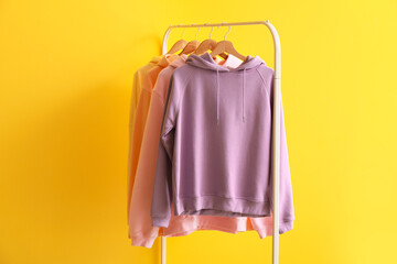 Rack with modern hoodies on color background