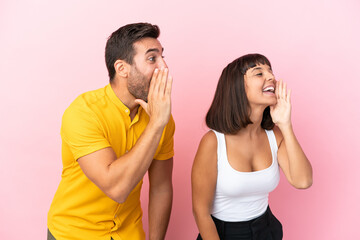 Young couple isolated on pink background shouting with mouth wide open to the lateral