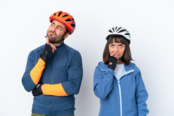 Young cyclist couple isolated on white background having doubts while looking up