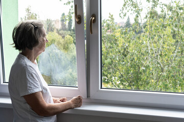 sad senior woman female alone home closeup depressed coronavirus isolation widower unhappy abandoned window