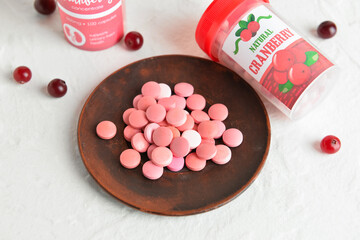 Plate with healthy cranberry pills on light background
