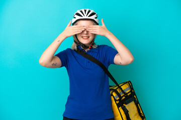 Young caucasian woman with thermal backpack isolated on blue background covering eyes by hands