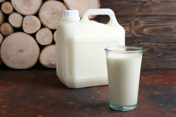 Gallon bottle and glass of milk on wooden background