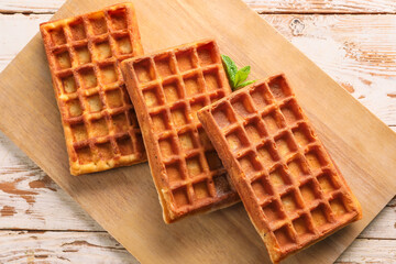 Board with delicious Belgian waffles on light wooden background
