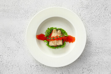 Plate of tasty sea bass fish with red caviar on light background