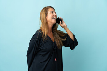 Middle age brazilian woman isolated on blue background keeping a conversation with the mobile phone