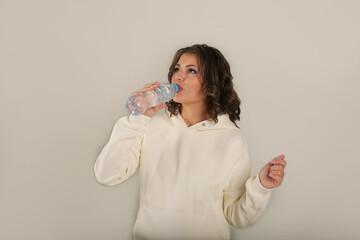 a young beautiful brown-haired girl in a warm milk-colored suit from a footer drinks water from a bottle