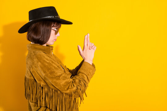 Photo of confident strong woman dressed cowboy clothes spectacles cap ready shoot empty space isolated yellow color background